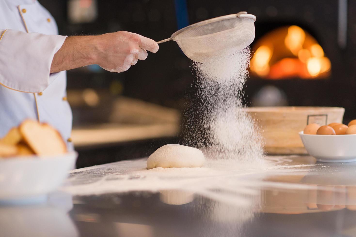 chef sprinkling flour over fresh pizza dough photo
