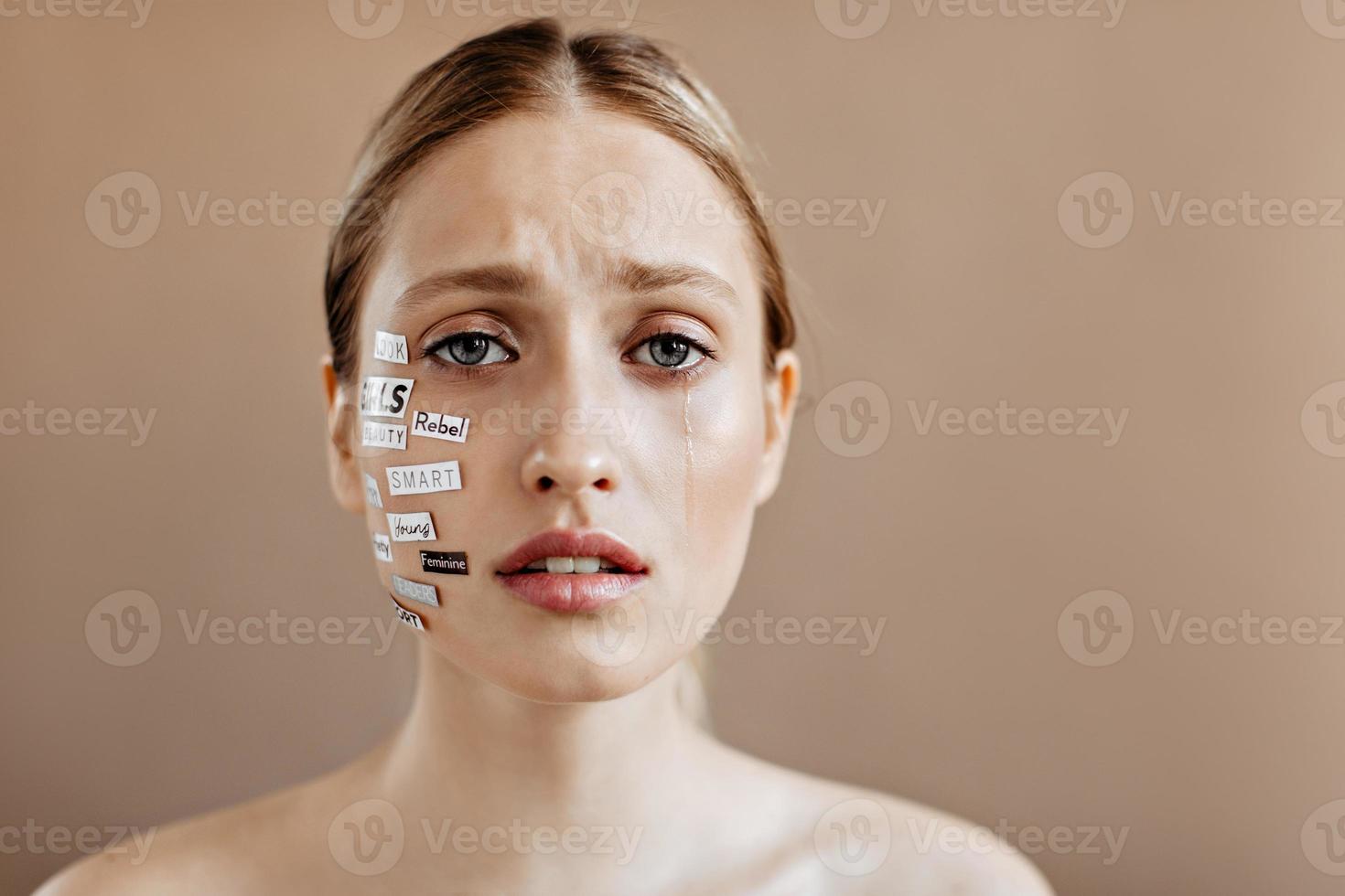 Close-up portrait of girl without makeup with bare shoulders and stickers on her face. Woman crying photo