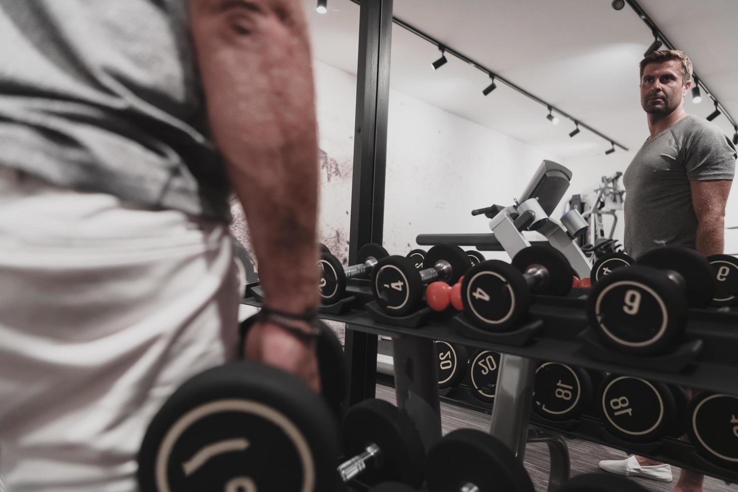 Struggling with age. Confident senior man exercising with dumbbells in health club. Selective focus photo