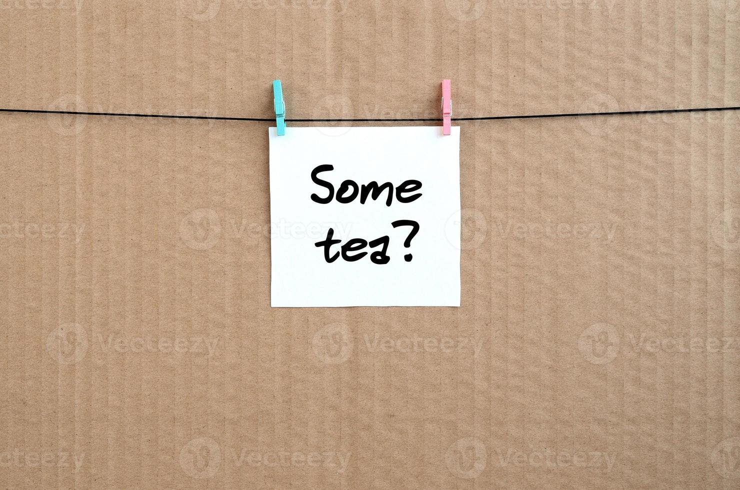 Some tea Note is written on a white sticker that hangs with a clothespin on a rope on a background of brown cardboard photo