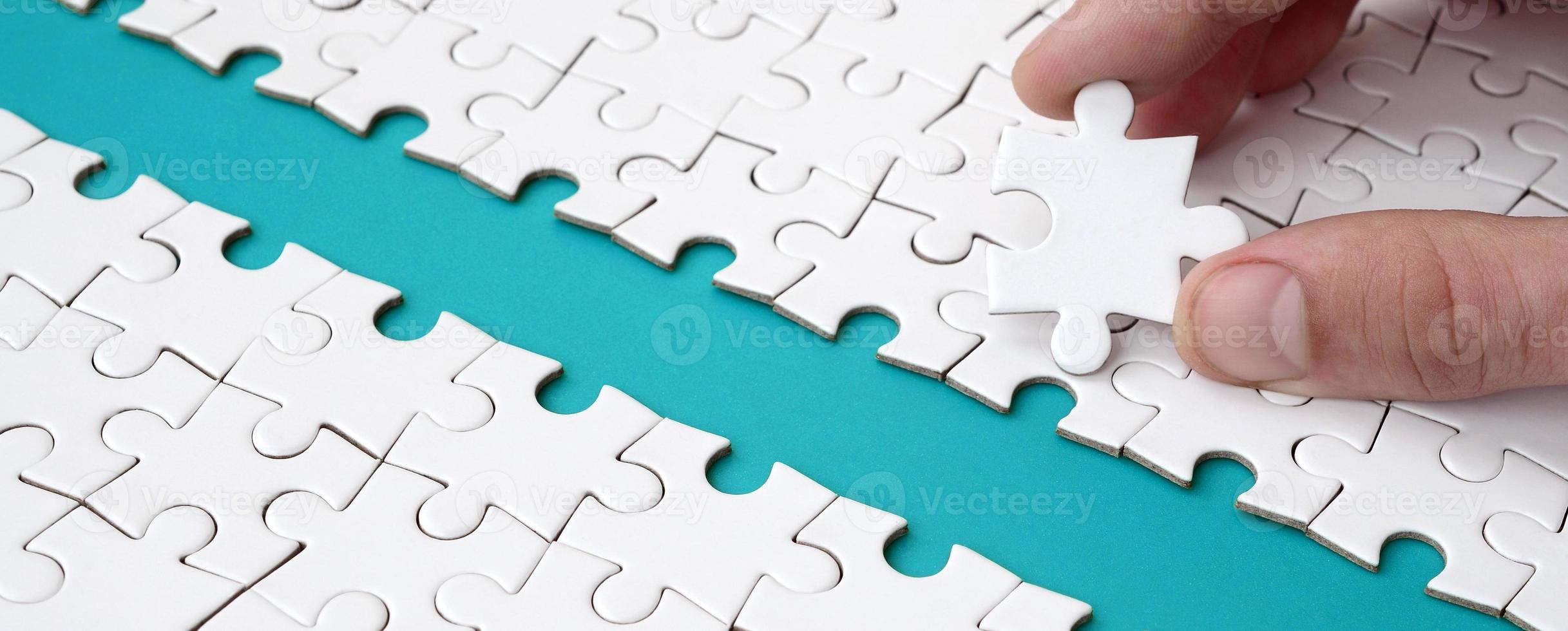 The human hand paves the way to the surface of the jigsaw puzzle, forming a blue space. The concept of overcoming the difficulties on the way to success photo