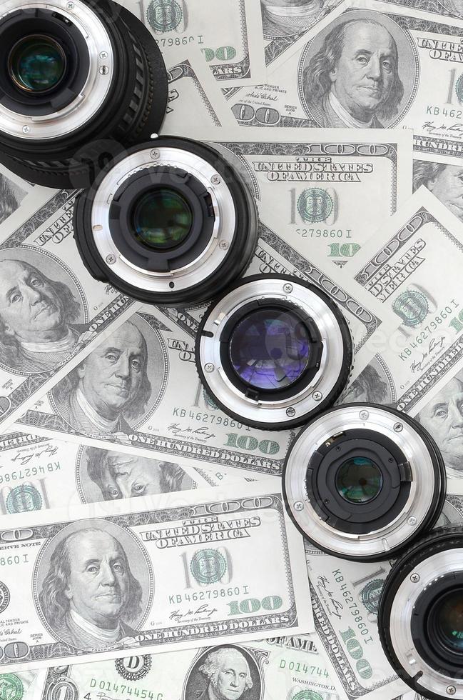 A few photographic lenses lies on the background of a lot of dollar bills. Space for text photo