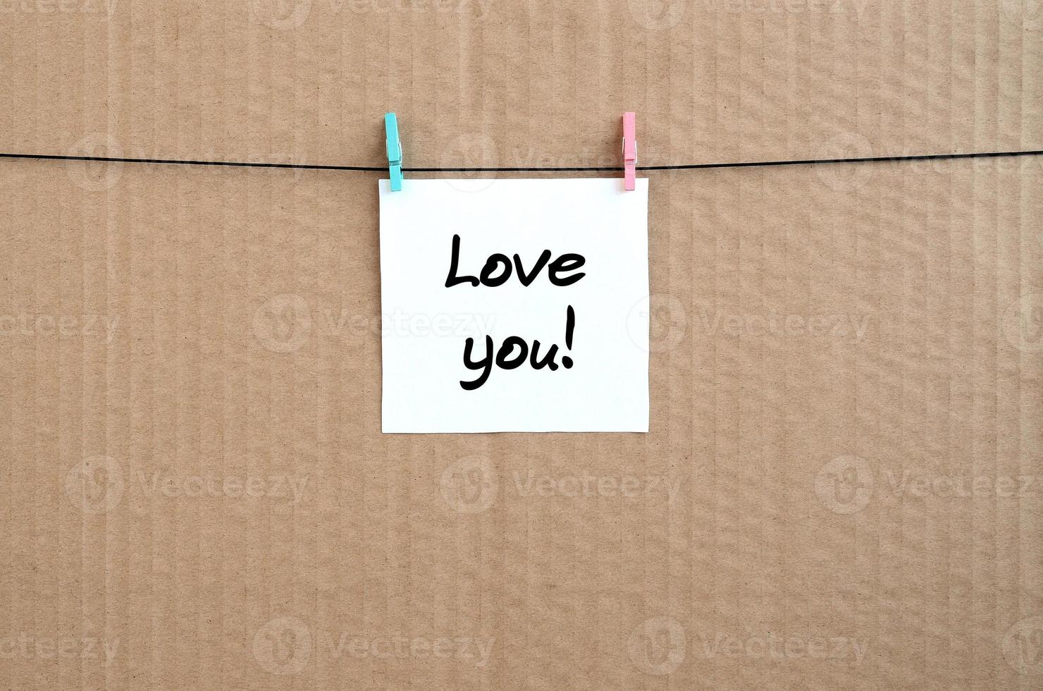 Love you Note is written on a white sticker that hangs with a clothespin on a rope on a background of brown cardboard photo