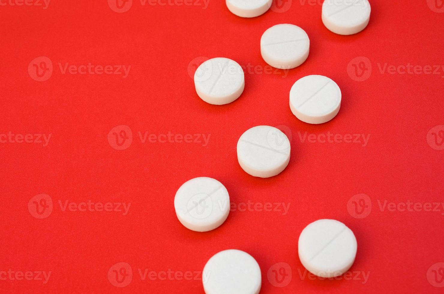 A few white tablets lie on a bright red background surface. Background image on medical and pharmaceutical topics photo