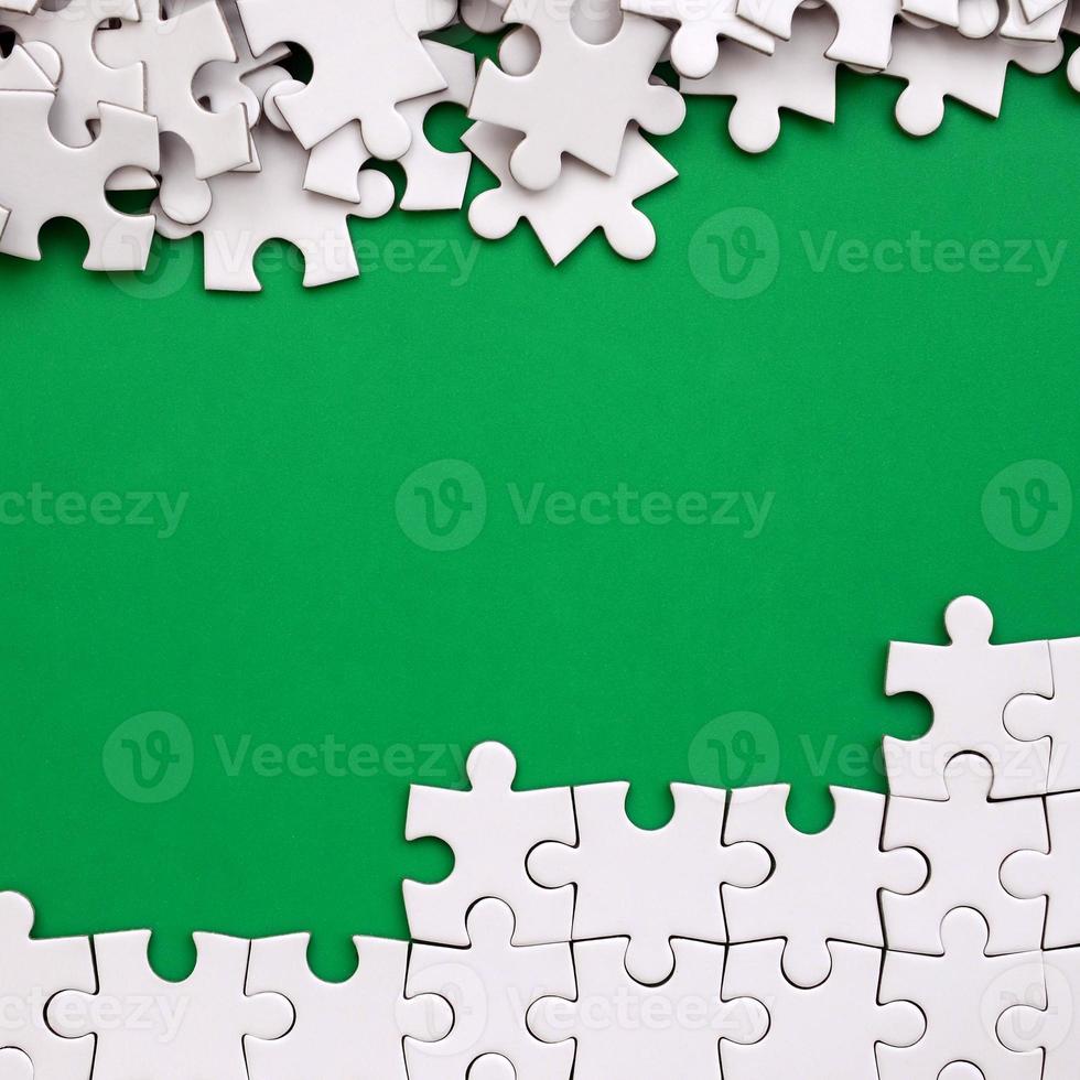 Fragment of a folded white jigsaw puzzle and a pile of uncombed puzzle elements against the background of a green surface. Texture photo with space for text