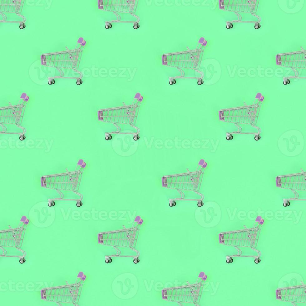 Shopping addiction, shopping lover or shopaholic concept. Many small empty shopping carts perform a pattern on a pastel colored paper background. Flat lay composition, top view photo