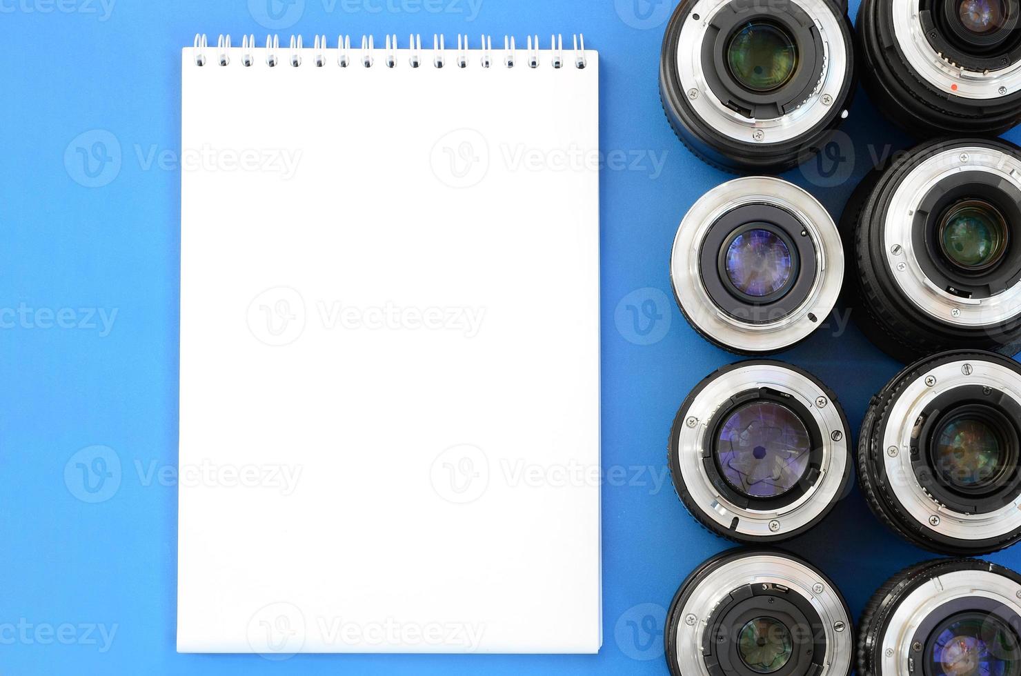 Several photographic lenses and white notebook lie on a bright blue background. Space for text photo