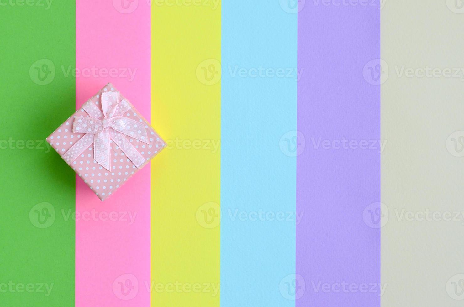 Small pink gift box lie on texture background of fashion pastel pink, blue, green, yellow, violet and beige colors paper in minimal concept. Abstract trendy pattern photo