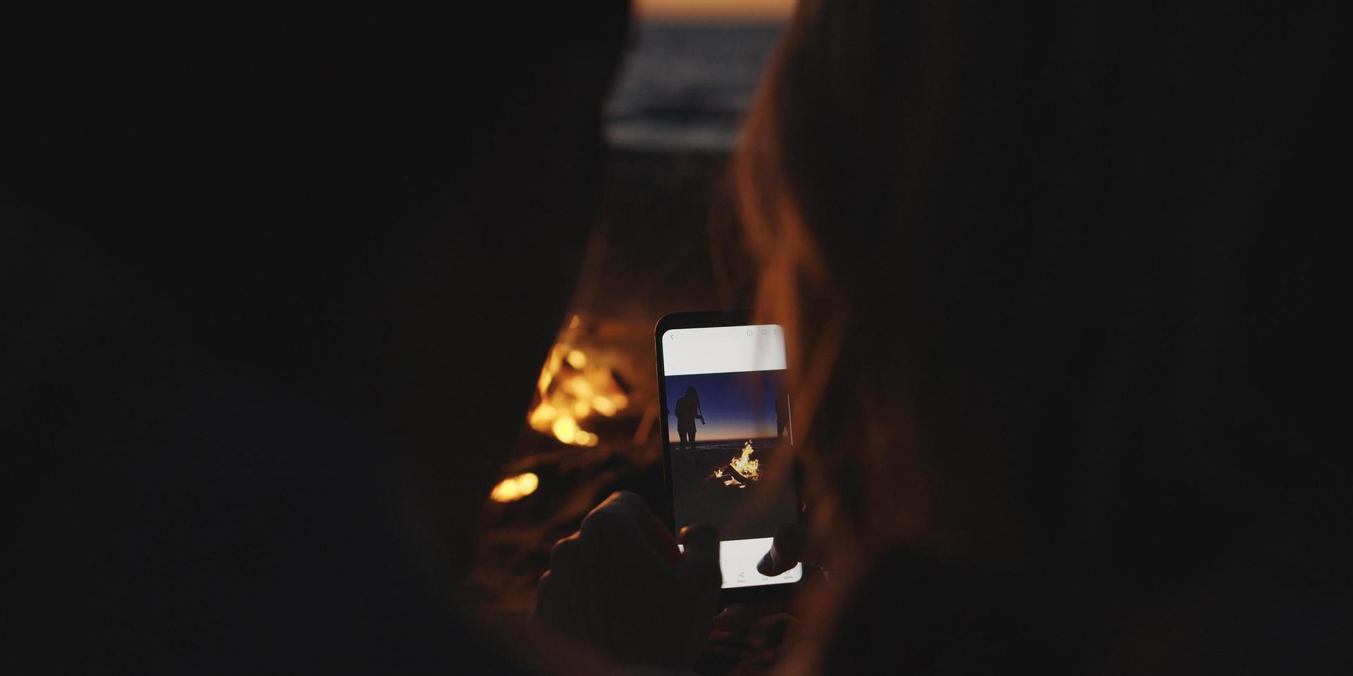 Couple taking photos beside campfire on beach