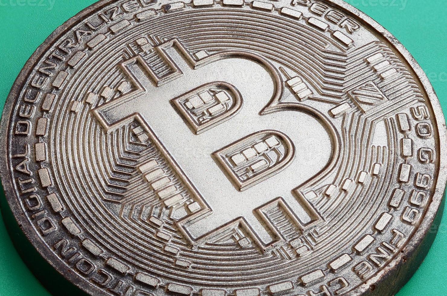 Chocolate product in the form of physical bitcoin lies on a green plastic background. Model of the crypto currency in the edible form photo