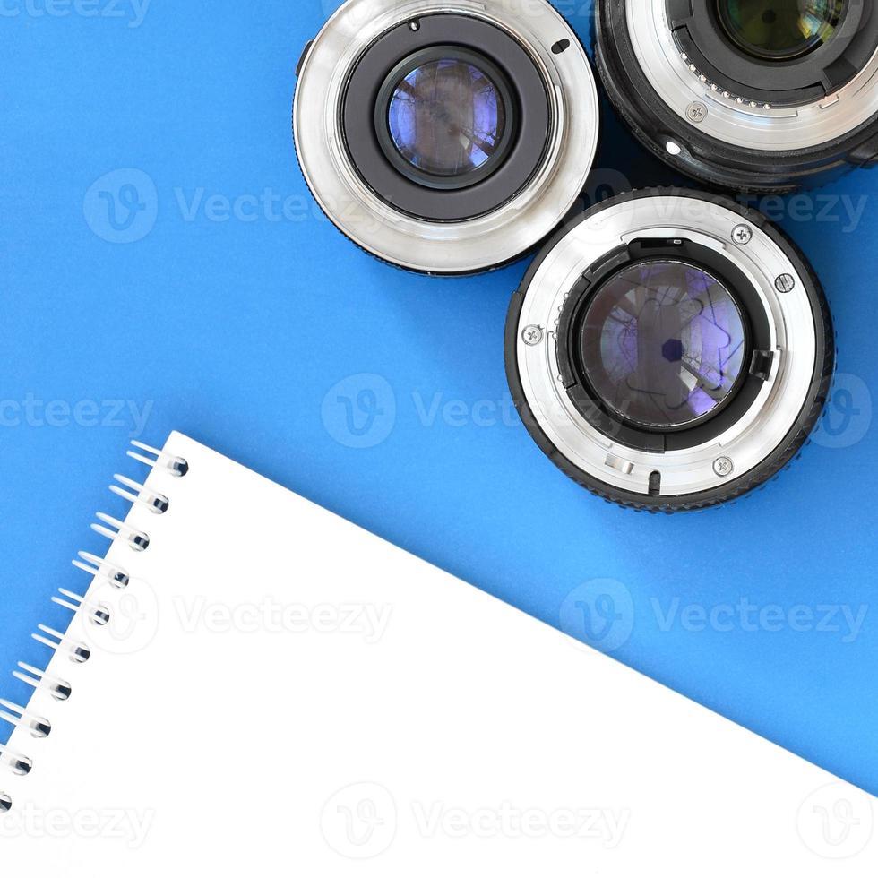 Several photographic lenses and white notebook lie on a bright blue background. Space for text photo