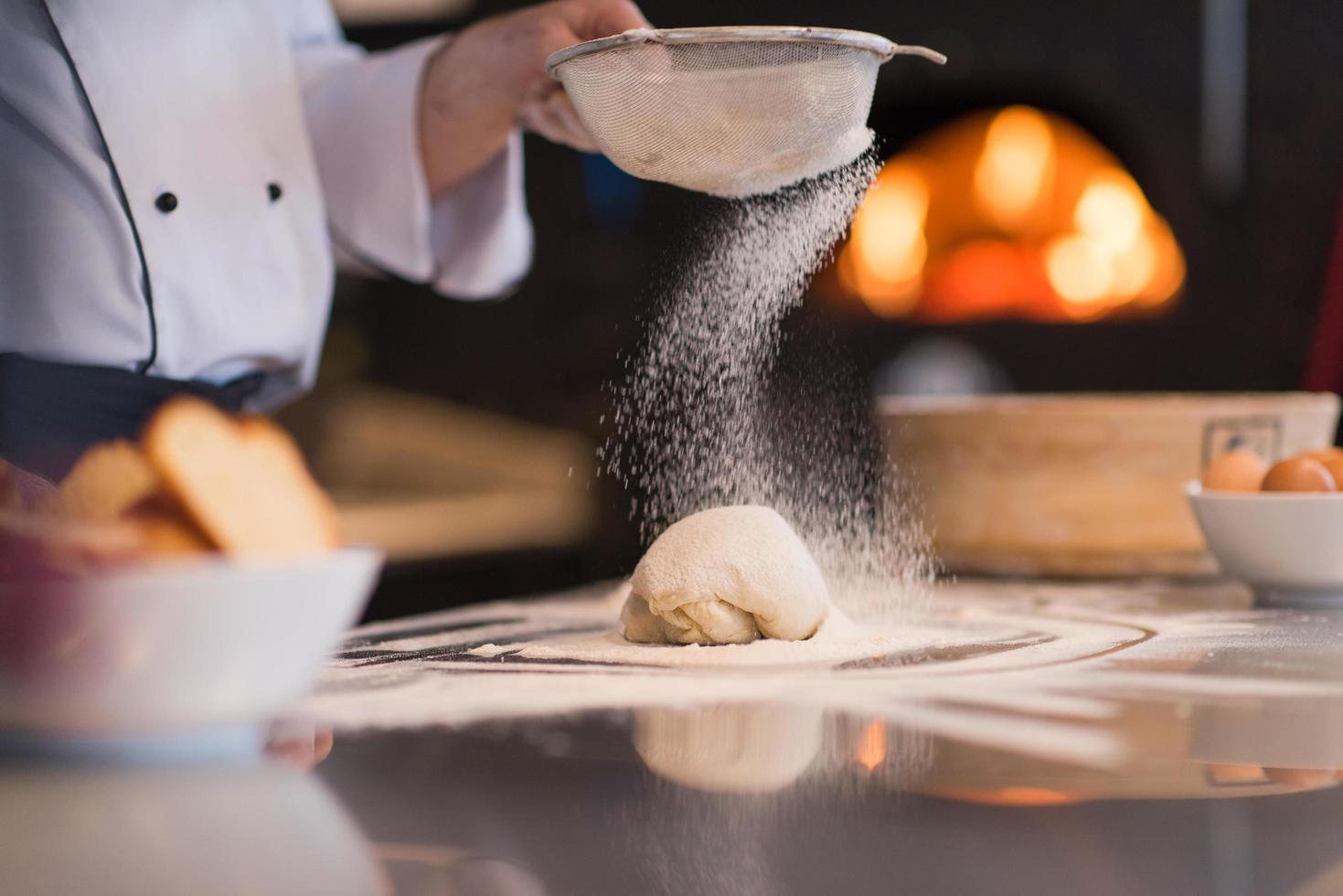 chef sprinkling flour over fresh pizza dough photo