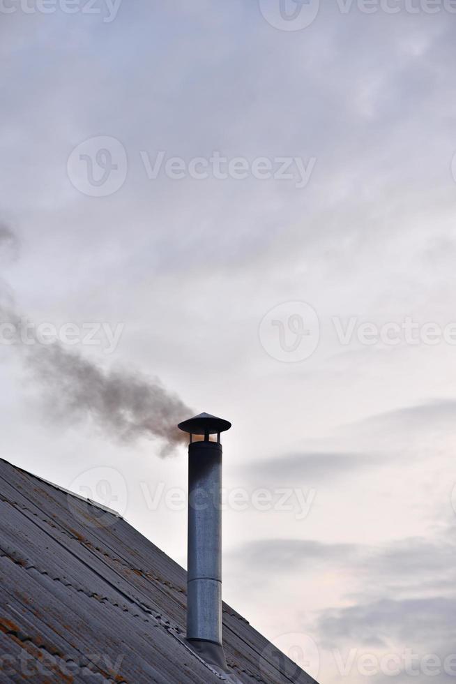 The smoking iron chimney of an old house in the evening. photo