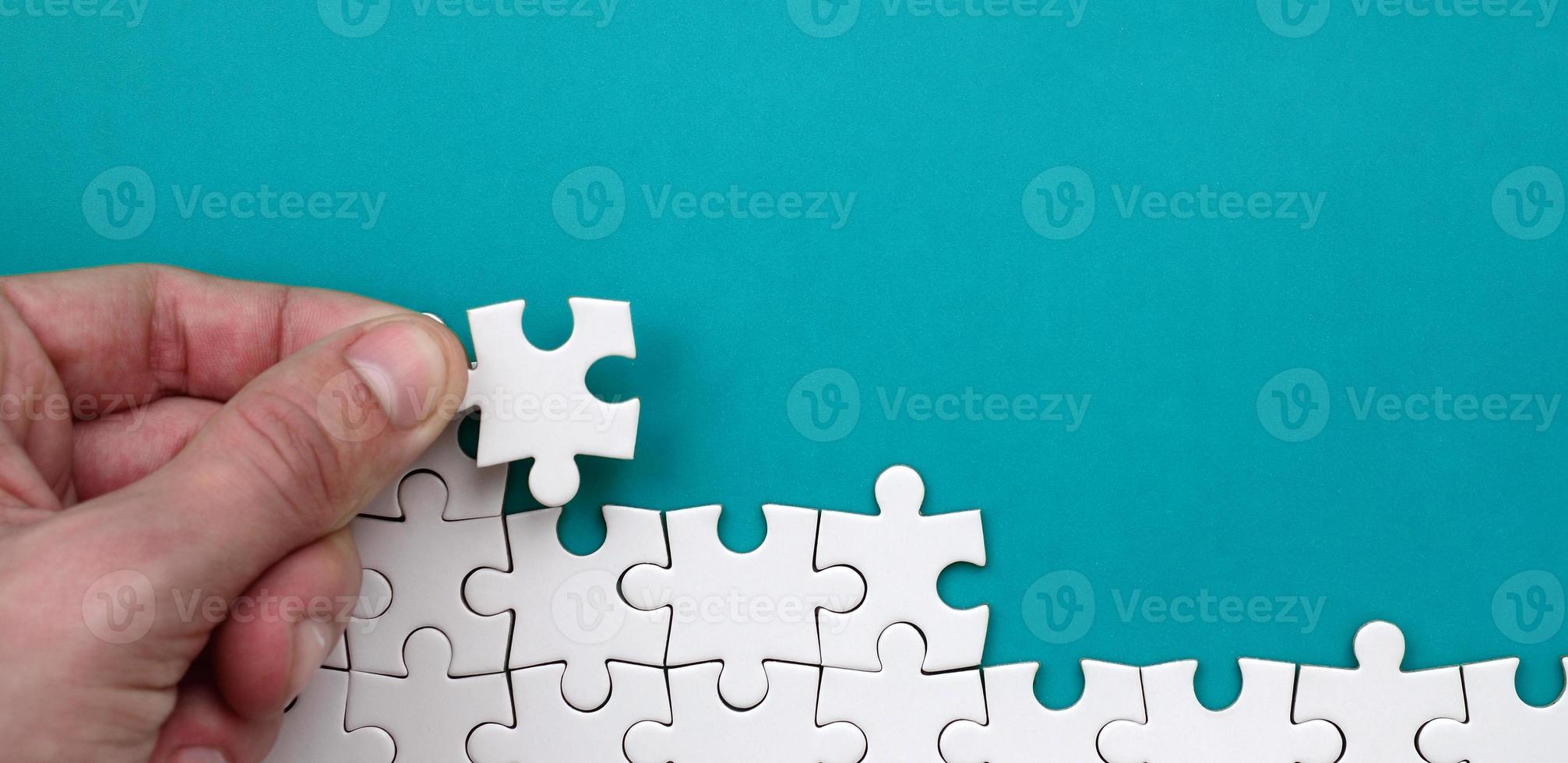 The hand folds a white jigsaw puzzle against the background of the blue surface. Texture photo with space for text