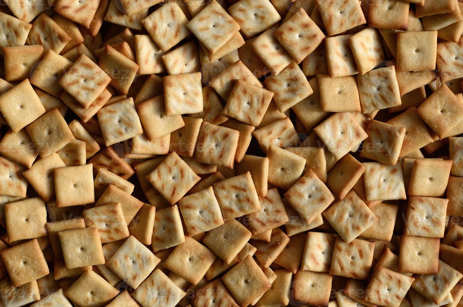 A lot of small cookies are square shaped. A pattern of a yellow salt cracker. Background image with salted pastry photo