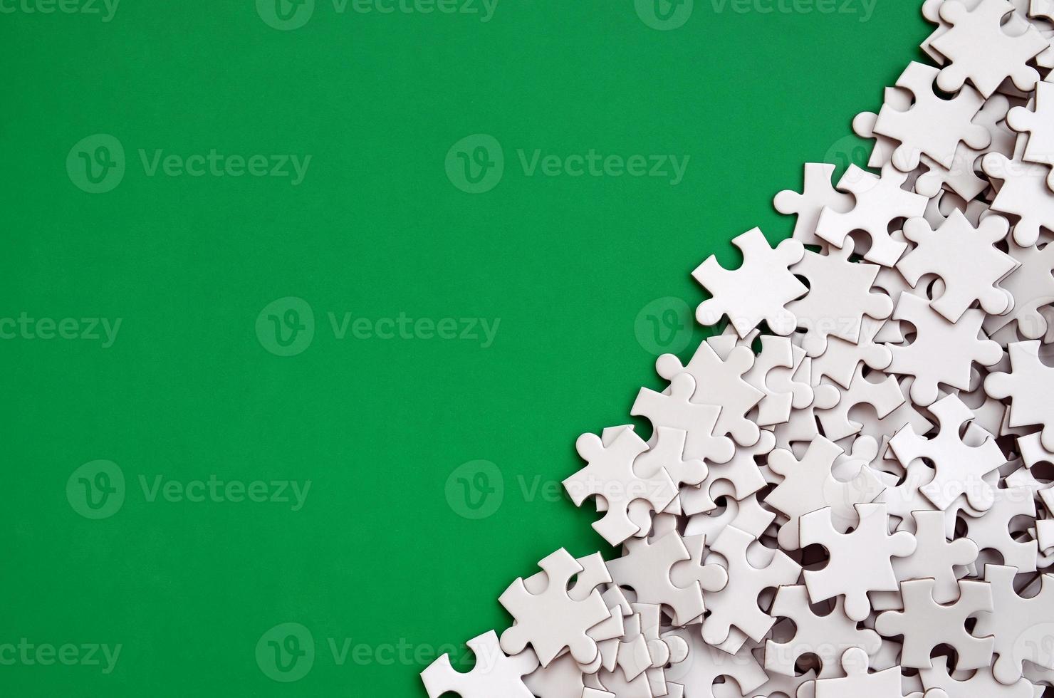 A pile of uncombed elements of a white jigsaw puzzle lies on the background of a green surface. Texture photo with copy space for text