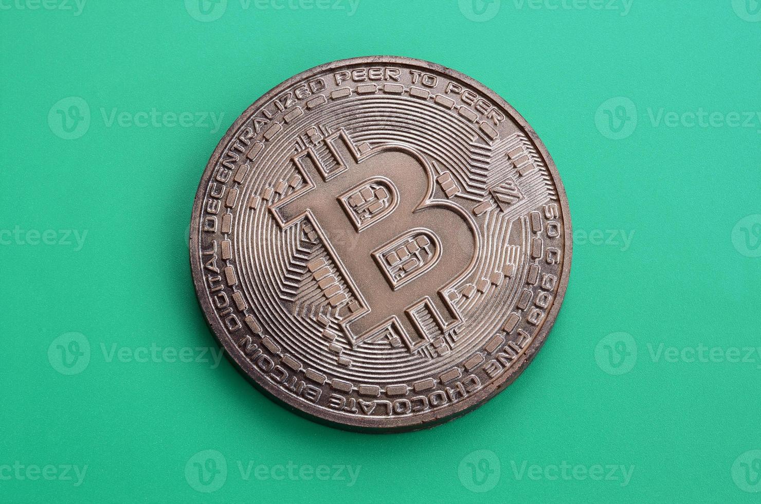 Chocolate product in the form of physical bitcoin lies on a green plastic background. Model of the crypto currency in the edible form photo
