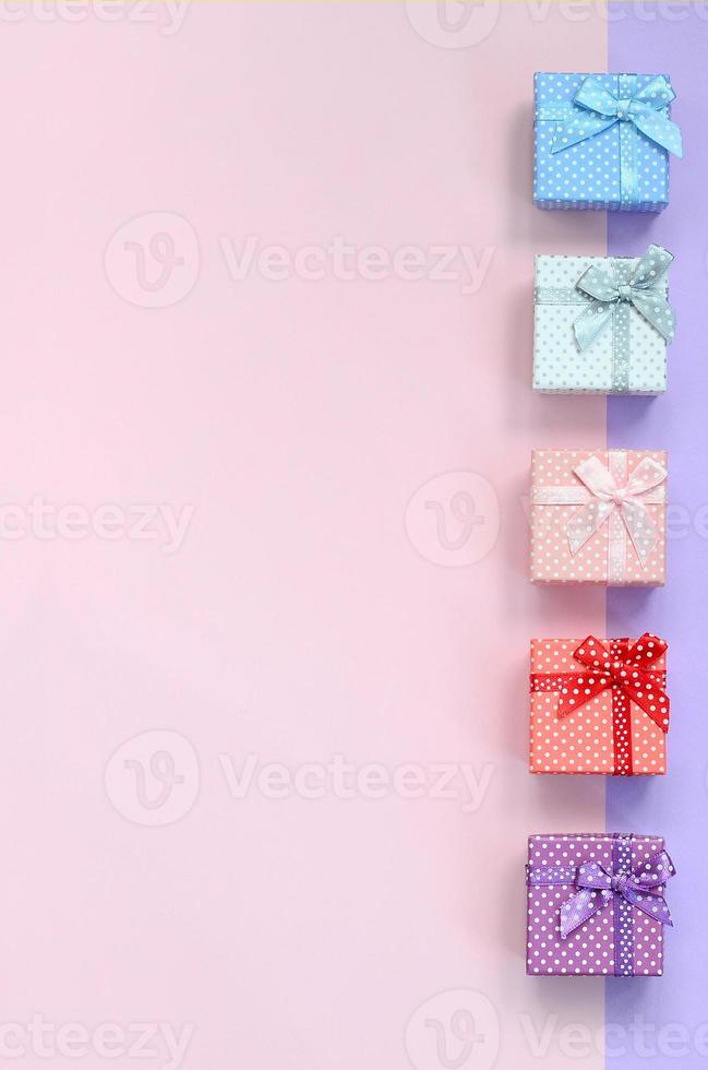 Small gift boxes of different colors with ribbons lies on a violet and pink color background photo