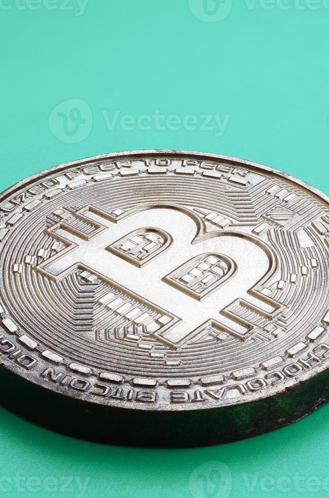Chocolate product in the form of physical bitcoin lies on a green plastic background. Model of the crypto currency in the edible form photo