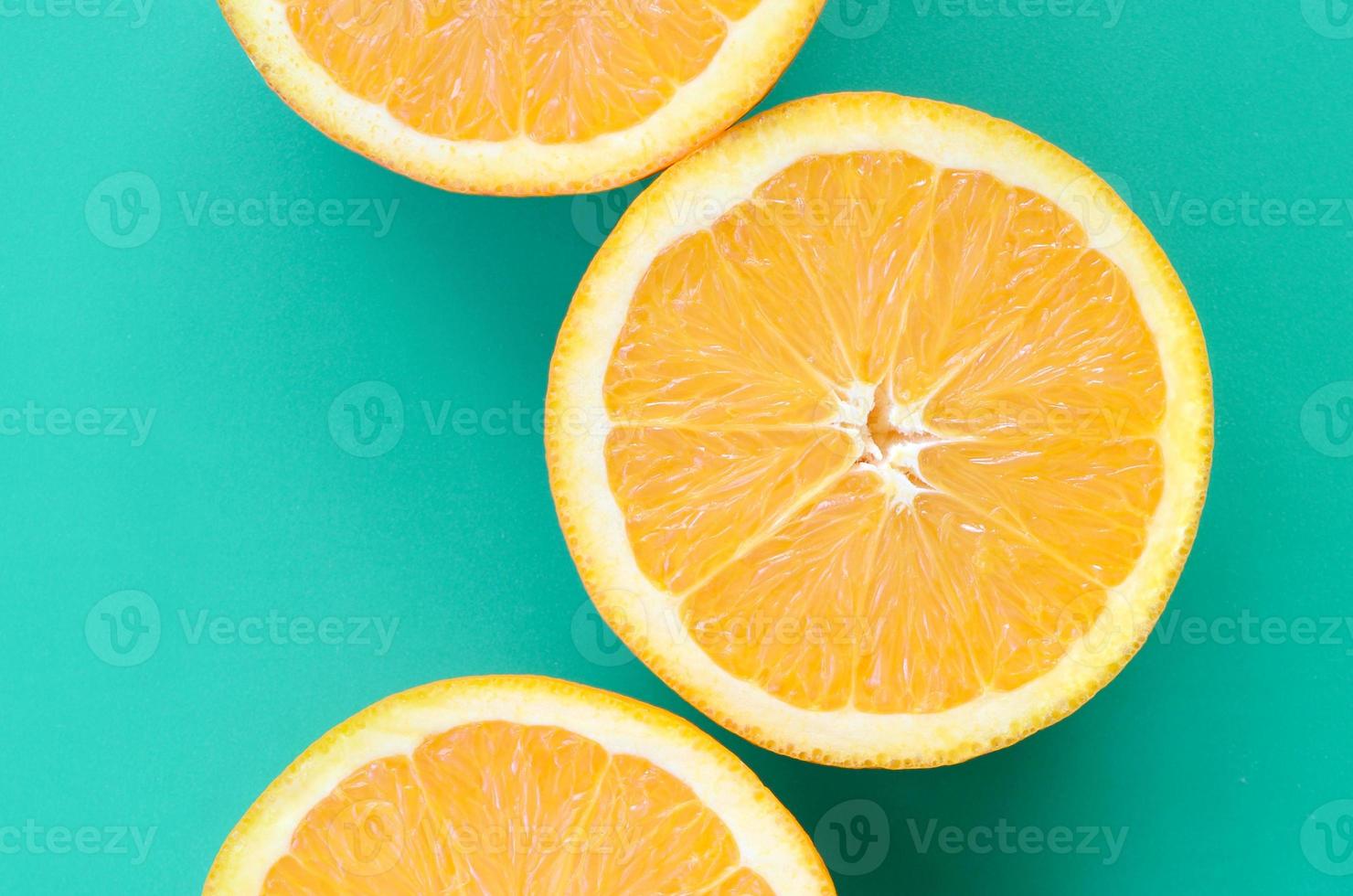 Top view of a several orange fruit slices on bright background in turquoise green color. A saturated citrus texture image photo