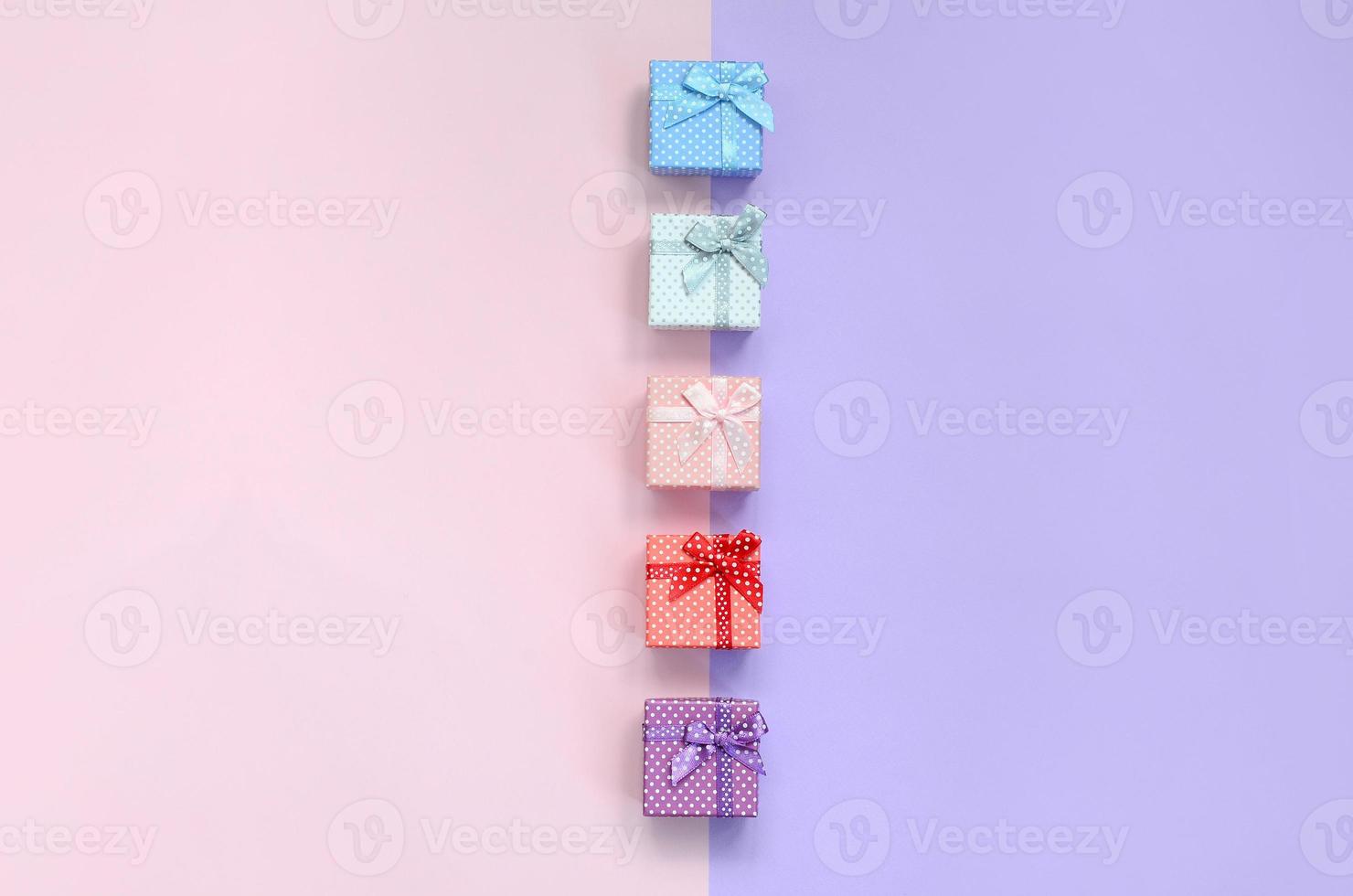 Small gift boxes of different colors with ribbons lies on a violet and pink color background photo