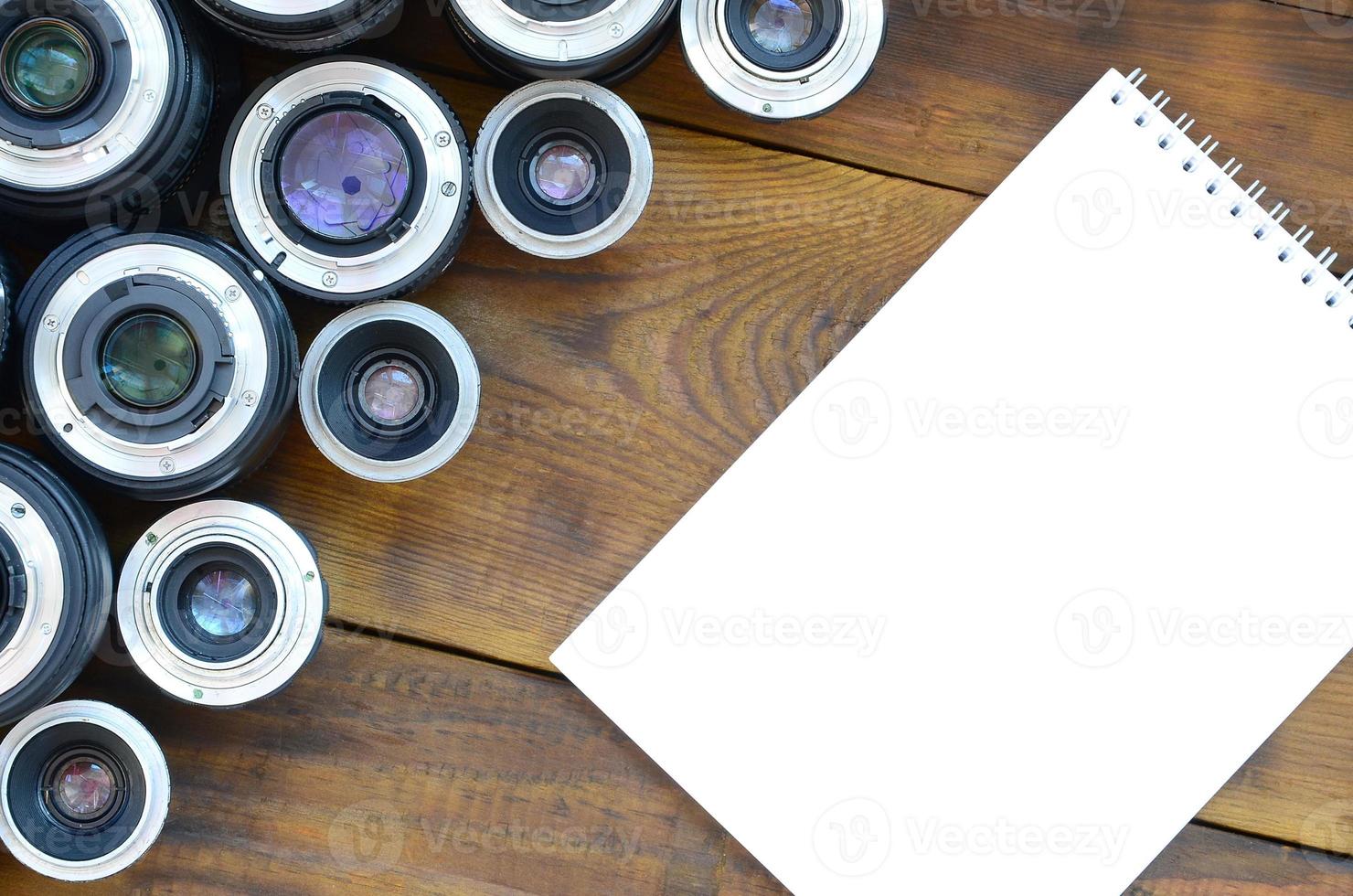 Several photographic lenses and white notebook lie on a brown wooden background. Space for text photo