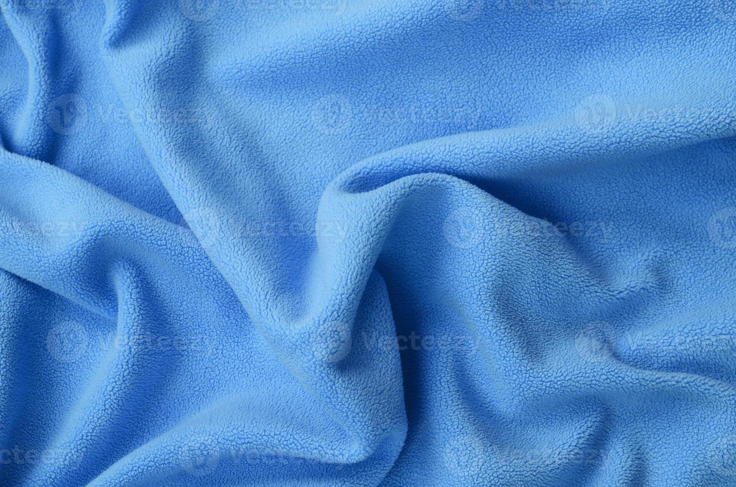 The blanket of furry blue fleece fabric. A background of light blue soft plush fleece material with a lot of relief folds photo