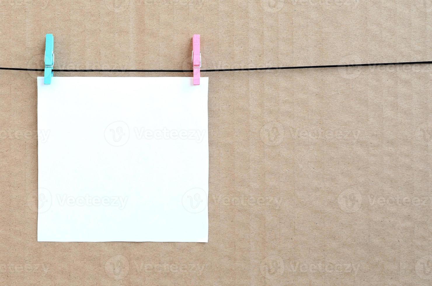 White blank card on rope on a brown cardboard background. Creative reminder, small sheet of paper on wooden clothespin, memo backdrop photo