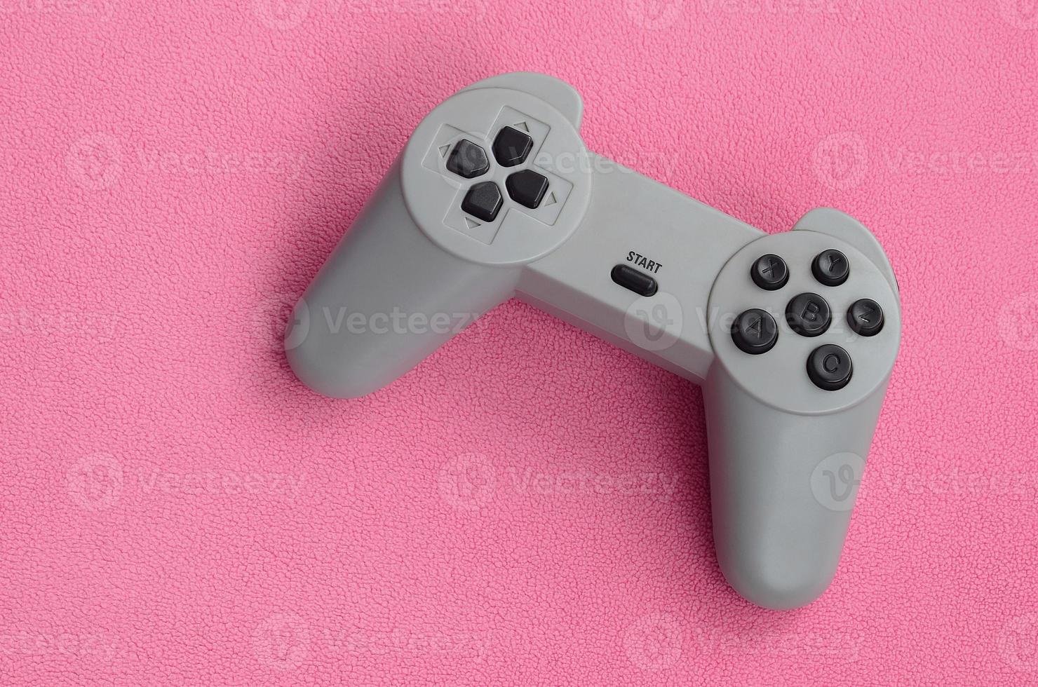 concepto de juegos. El joystick de una sola almohadilla se encuentra sobre la manta de tela de lana rosa peluda. controlador para videojuegos en una textura de fondo de material de vellón de felpa suave rosa claro foto