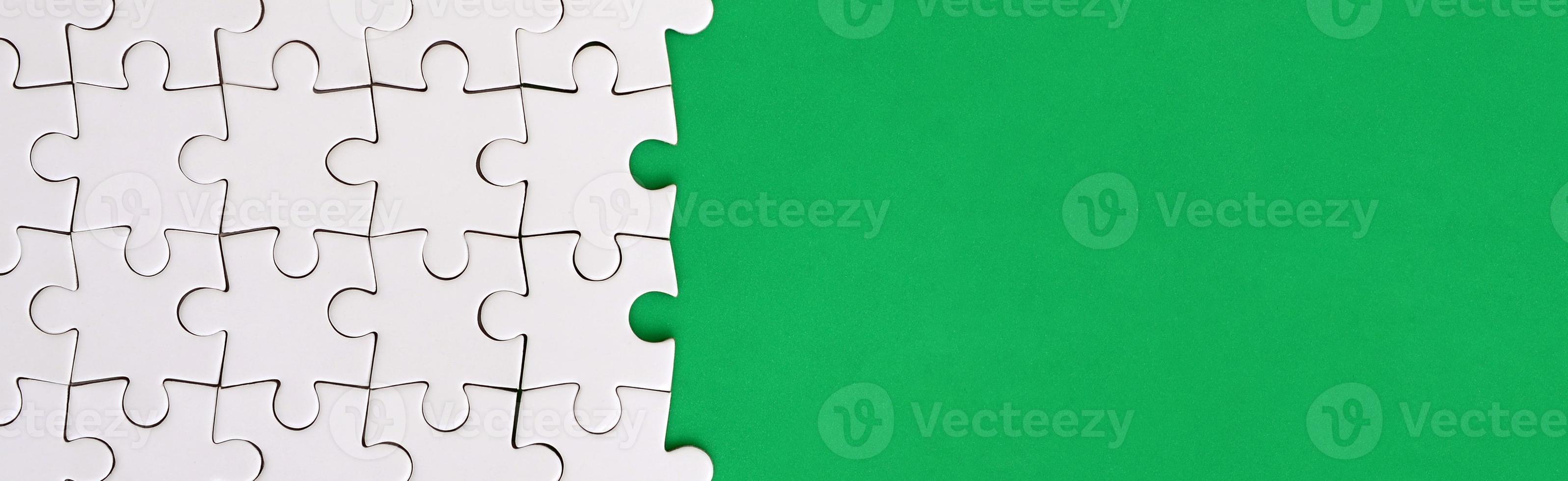 Fragment of a folded white jigsaw puzzle on the background of a green plastic surface. Texture photo with copy space for text