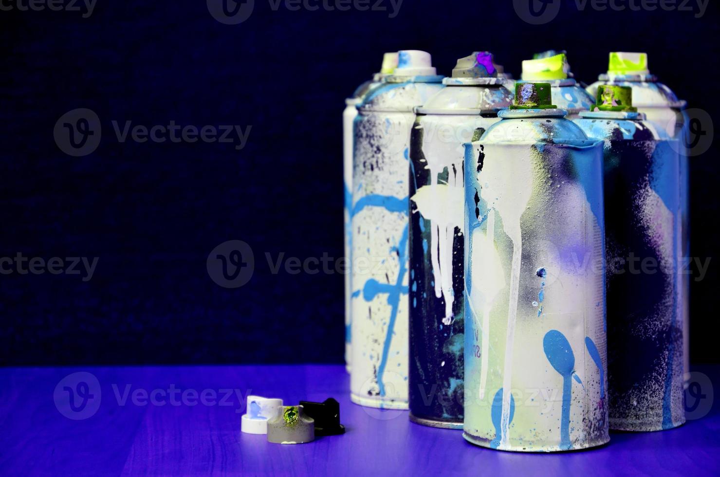 Still life with a large number of used colorful spray cans of aerosol paint lying on the treated wooden surface in the artist's graffiti workshop. Dirty and stained cans for spray art photo
