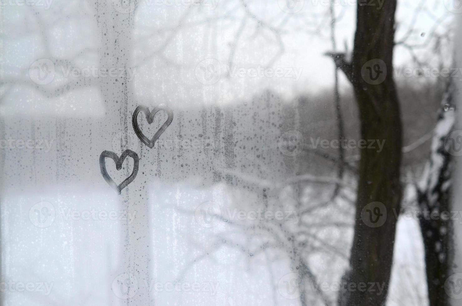 dos corazones pintados en un vidrio empañado en invierno foto