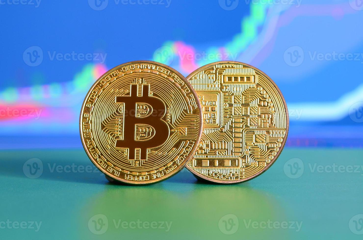 Two gold bitcoins lie on the green surface on the background of the display, which depicts the growth of the position on the chart photo