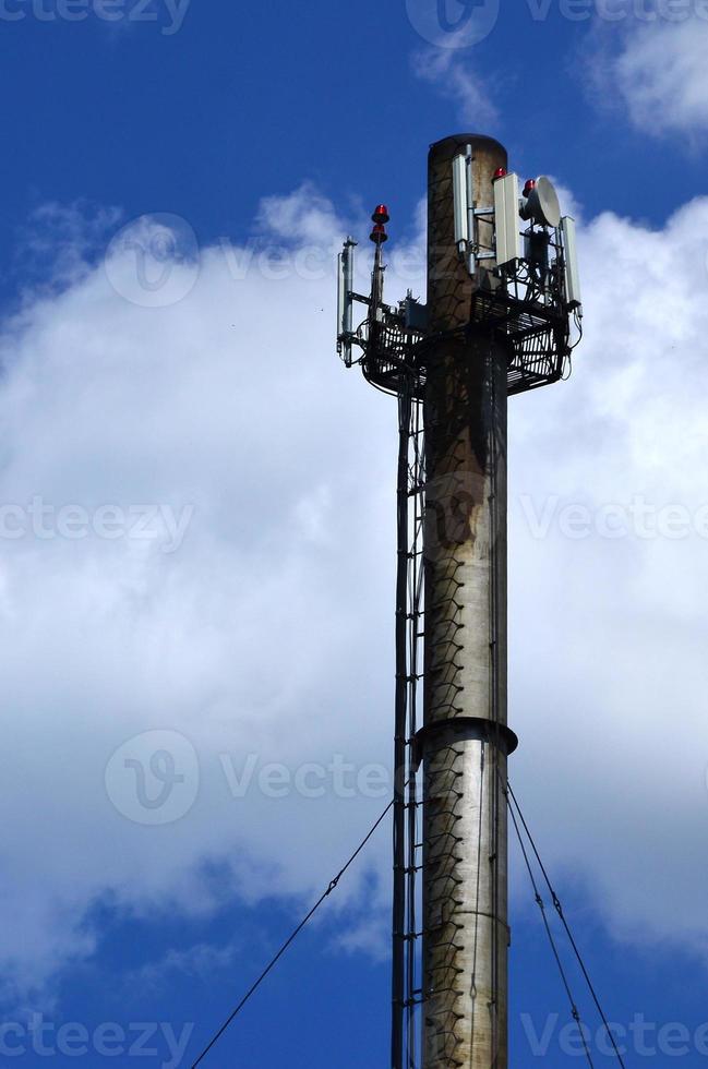 High metal chimney of industrial plant with ladder in the form of metal braces against the background of a cloudy blue sky photo