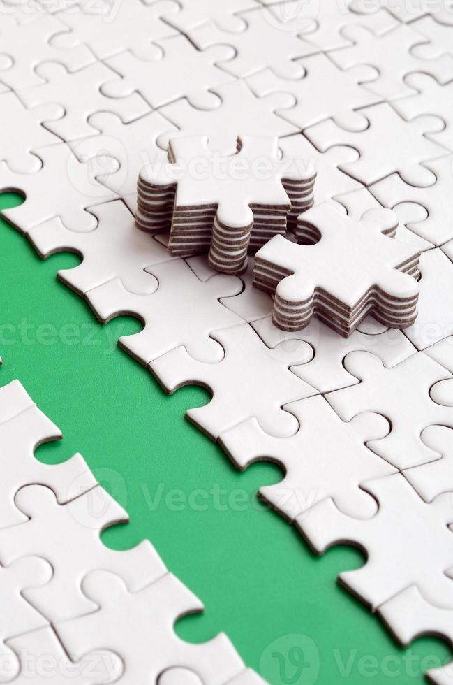 The green path is laid on the platform of a white folded jigsaw puzzle. The missing elements of the puzzle are stacked nearby. Texture image with space for text photo