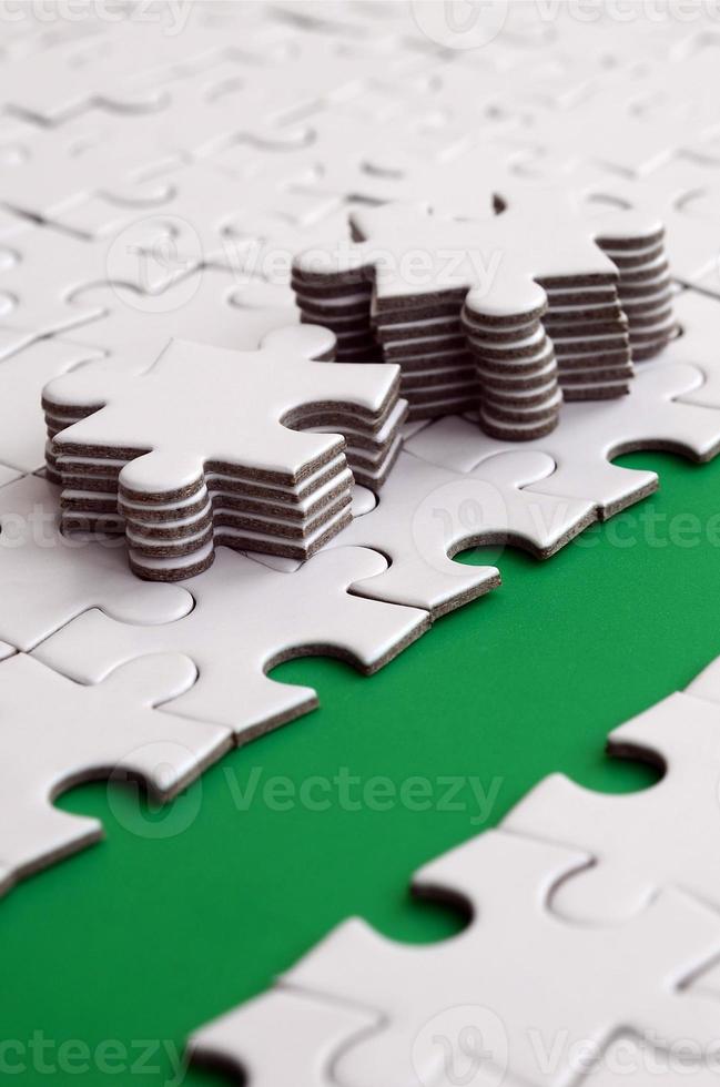 The green path is laid on the platform of a white folded jigsaw puzzle. The missing elements of the puzzle are stacked nearby. Texture image with space for text photo