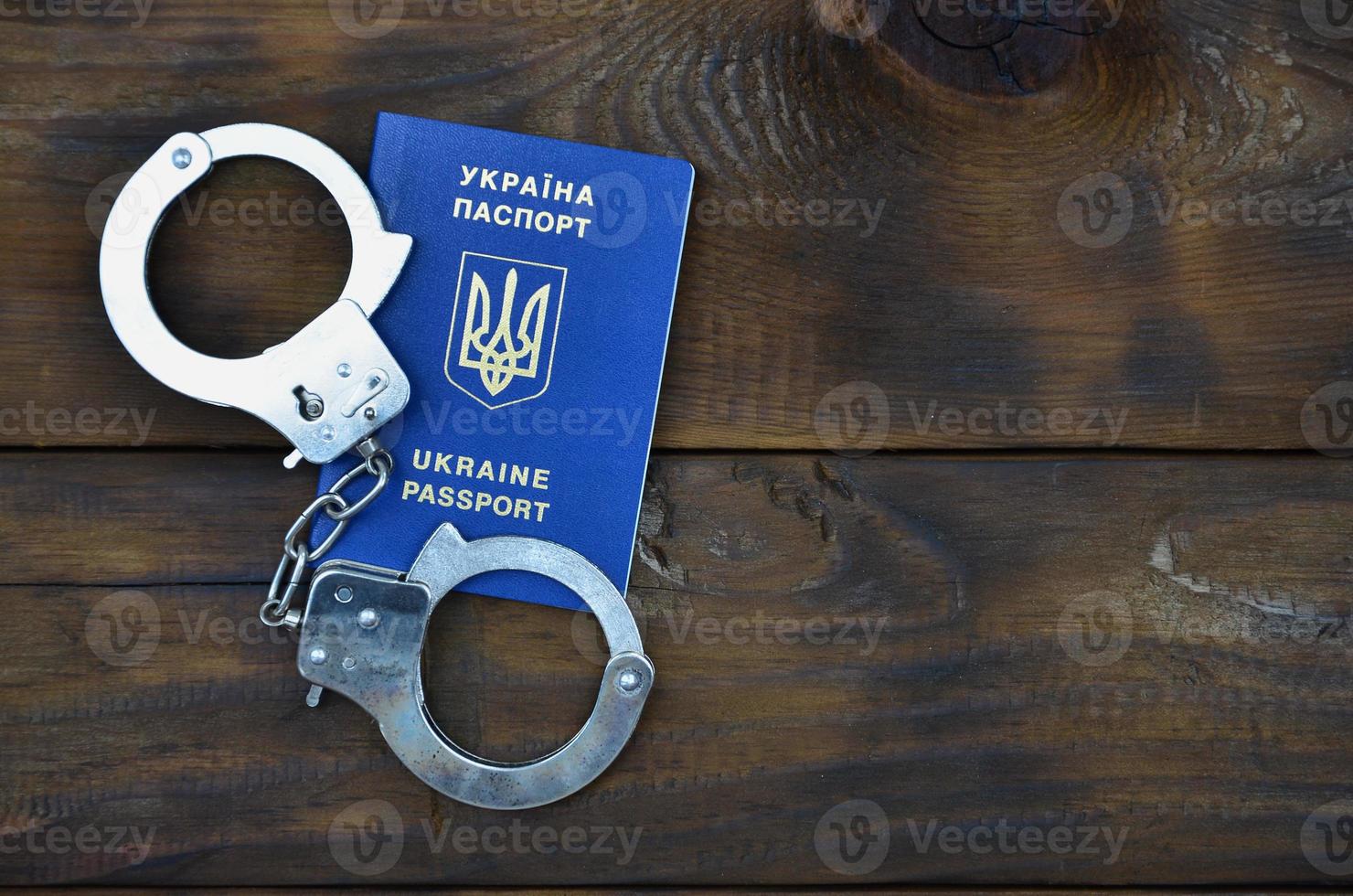 Ukrainian passport with police handcuffs lies on a wooden table. The concept of crime of Ukrainian citizens when traveling abroad. Illegal activities during travel photo