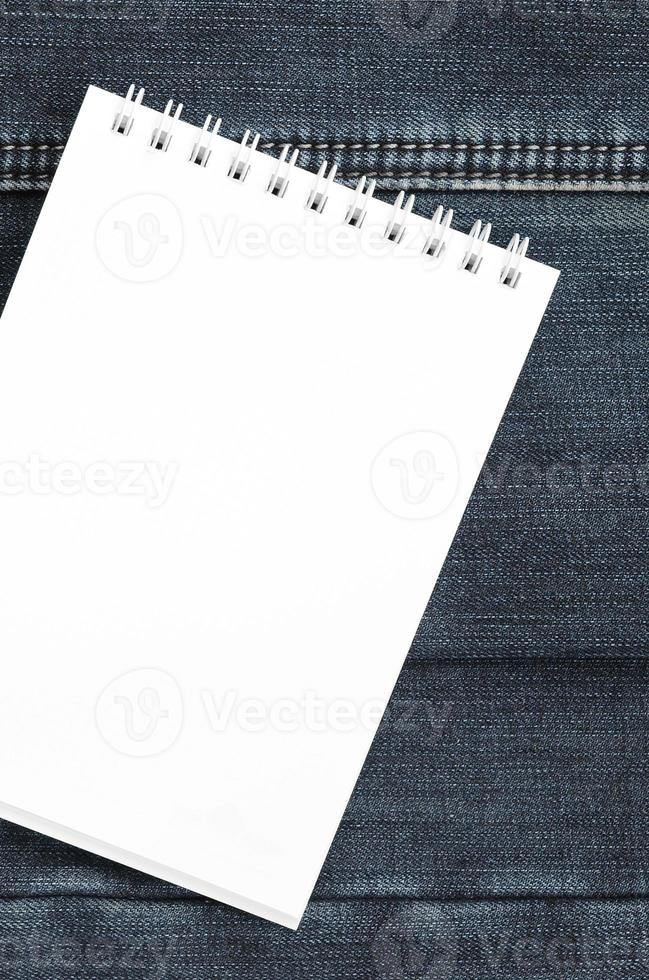 White notebook with clean pages lying on dark blue jeans background. Image with copy space photo