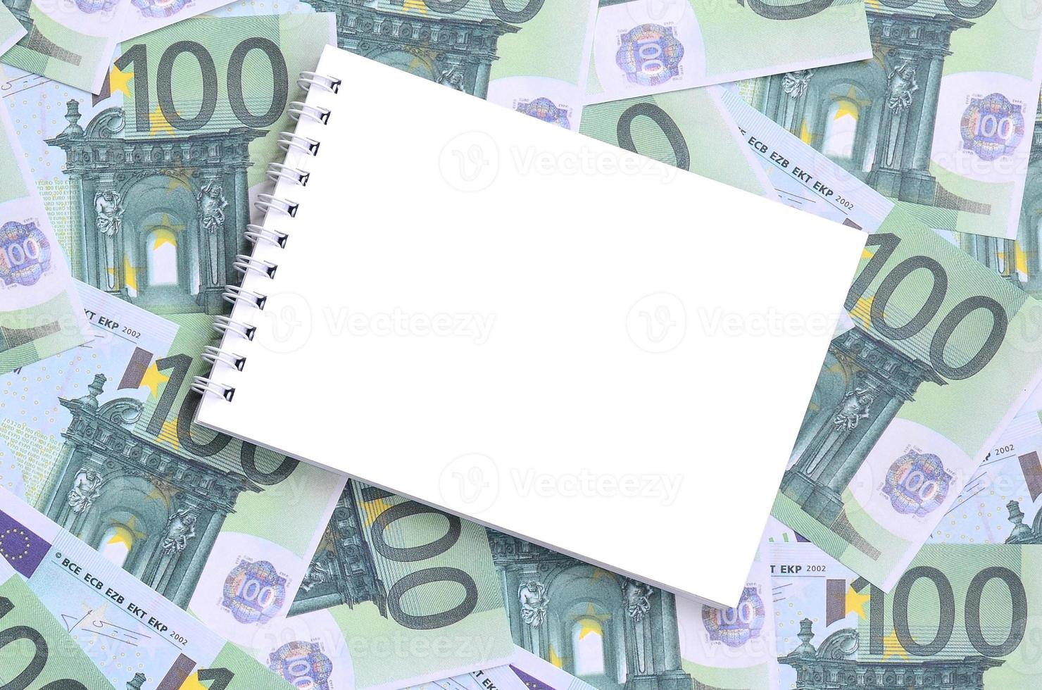 White notebook with clean pages lying on a set of green monetary denominations of 100 euros. A lot of money forms an infinite heap photo