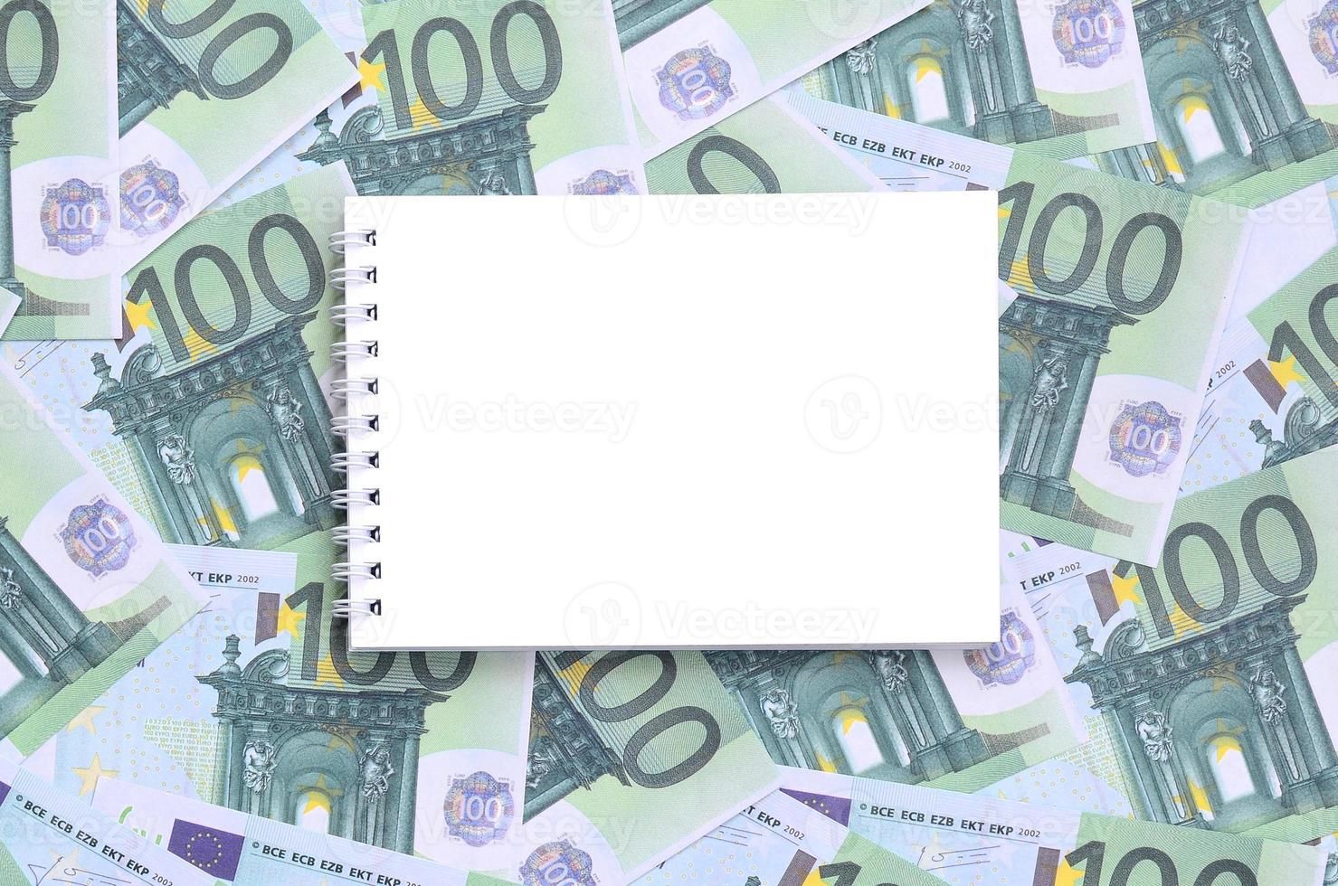 cuaderno blanco con páginas limpias sobre un conjunto de denominaciones monetarias verdes de 100 euros. mucho dinero forma un montón infinito foto