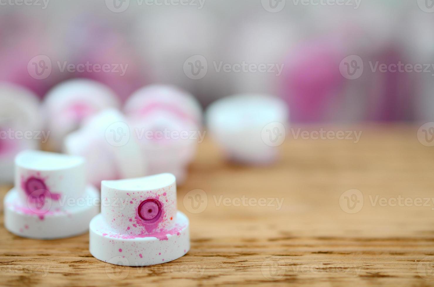 The soiled pink nozzles from the paint sprayer lies on a wooden plank on a background of a many dirty spray cans photo