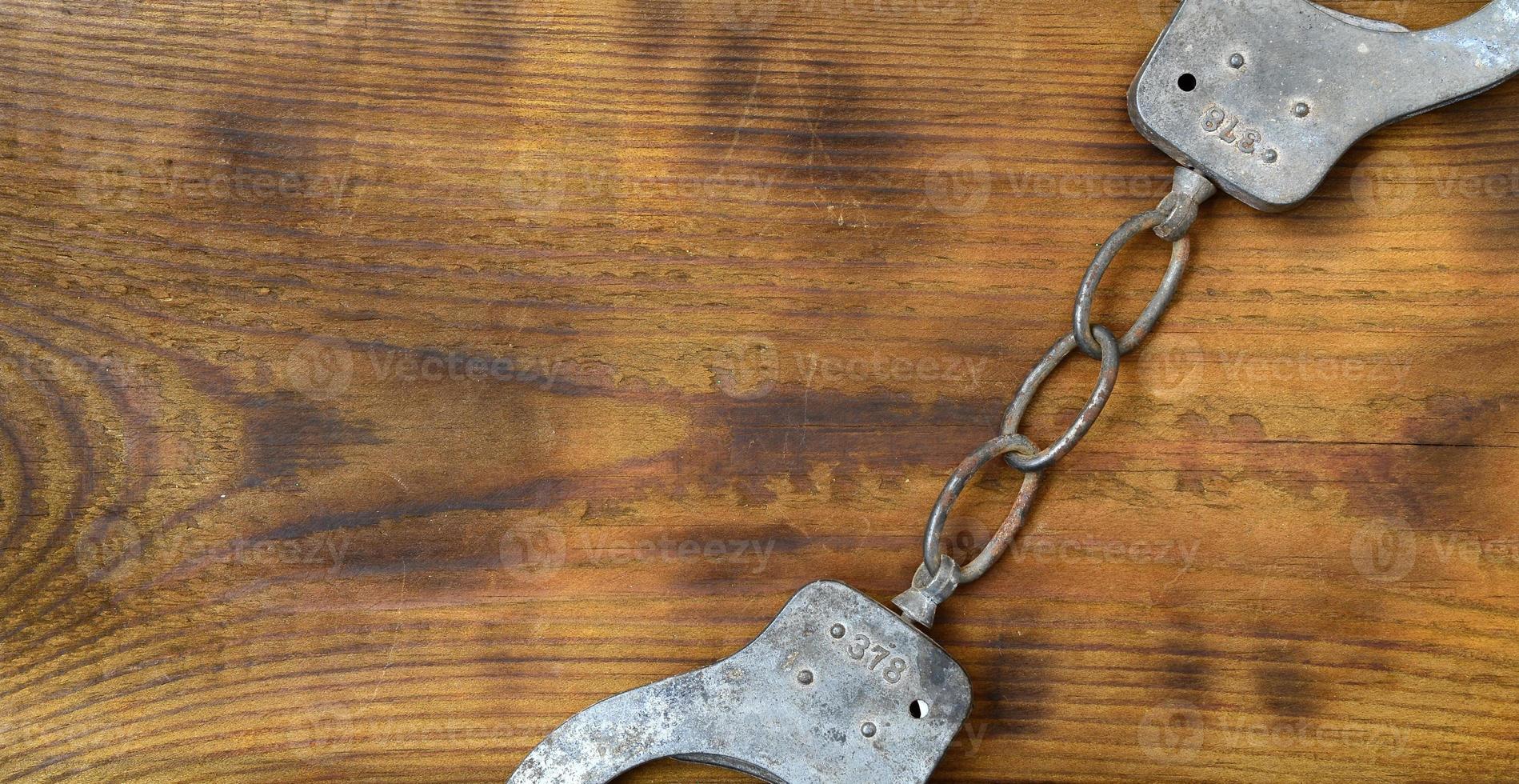 Old and rusty police handcuffs lie on a scratched wooden surface. The concept of an old crime photo