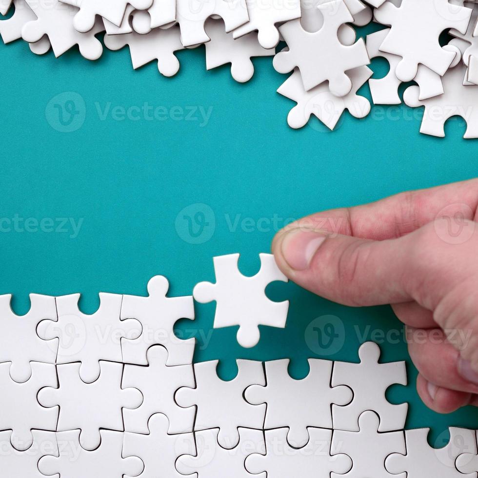 The hand folds a white jigsaw puzzle and a pile of uncombed puzzle pieces lies against the background of the blue surface. Texture photo with space for text
