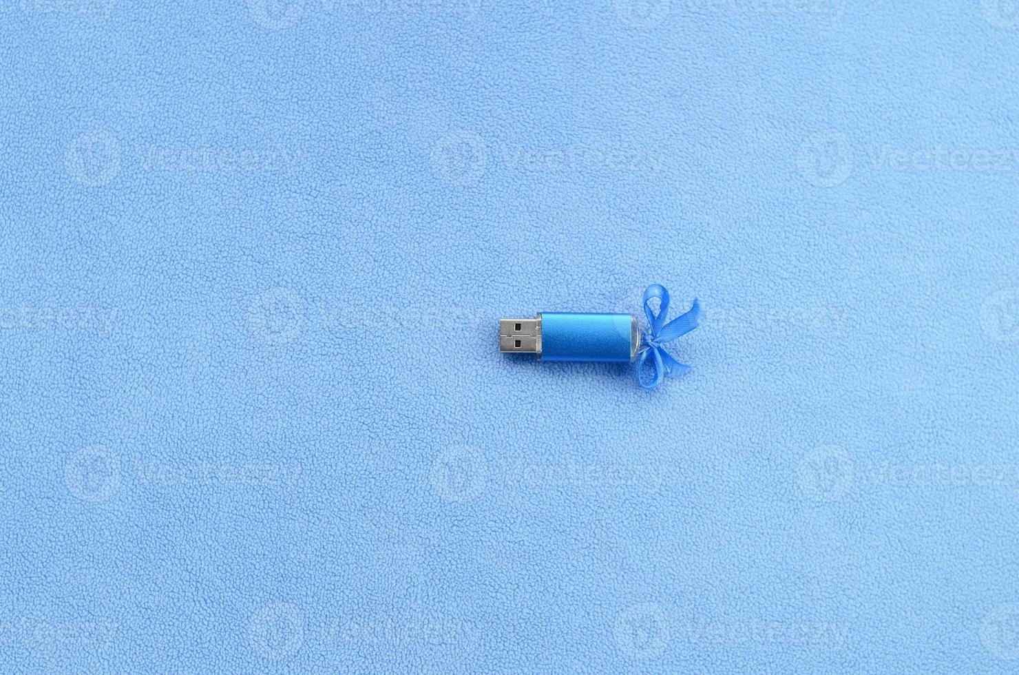 Brilliant blue usb flash memory card with a blue bow lies on a blanket of soft and furry light blue fleece fabric. Classic female gift design for a memory card photo