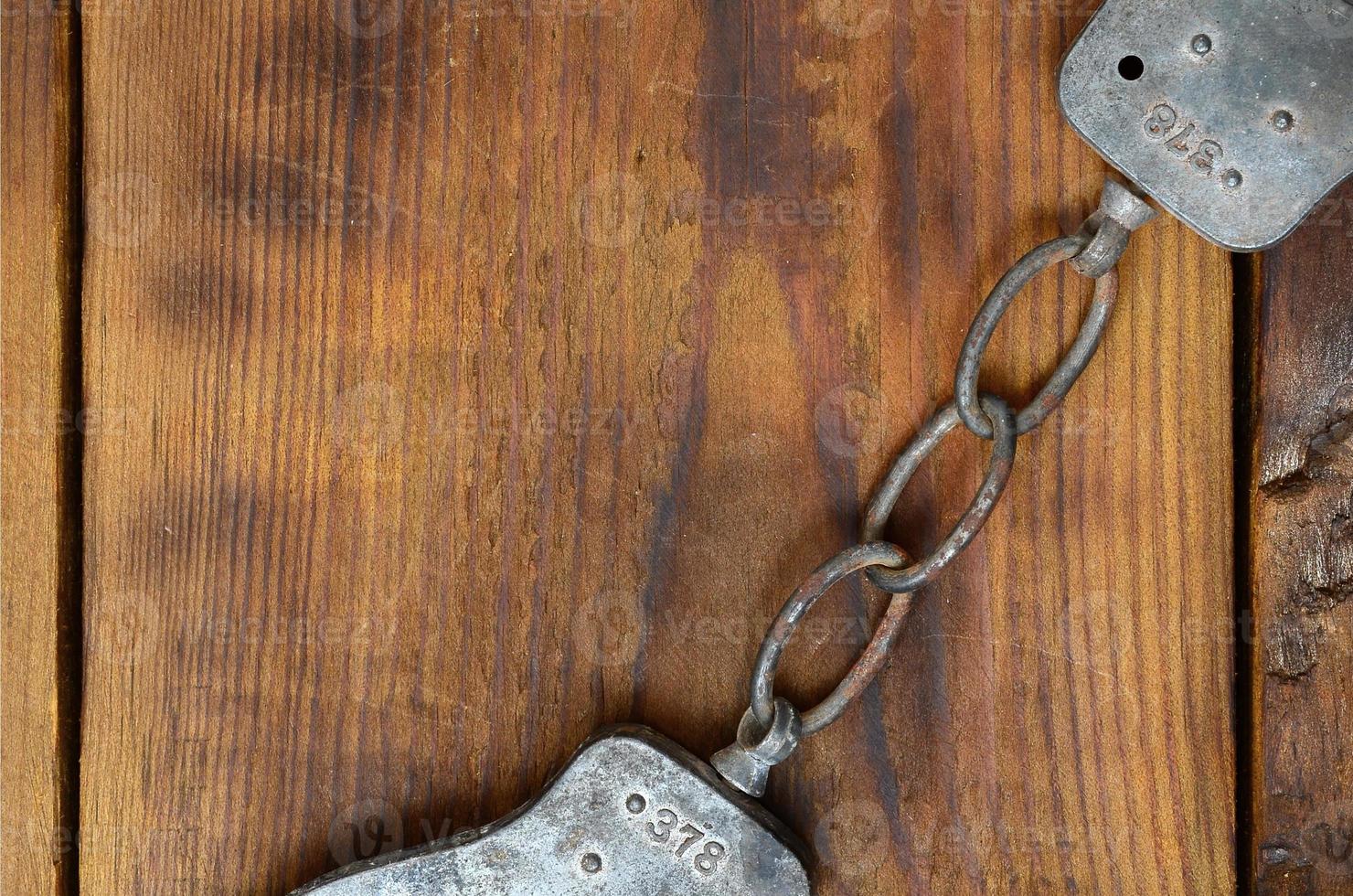 Old and rusty police handcuffs lie on a scratched wooden surface. The concept of an old crime photo