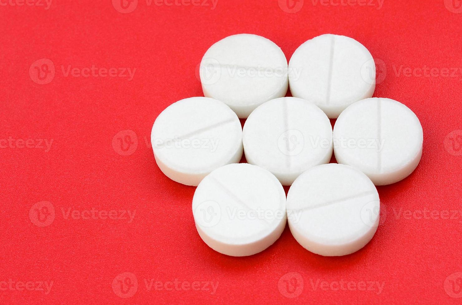 A few white tablets lie on a bright red background surface. Background image on medical and pharmaceutical topics photo
