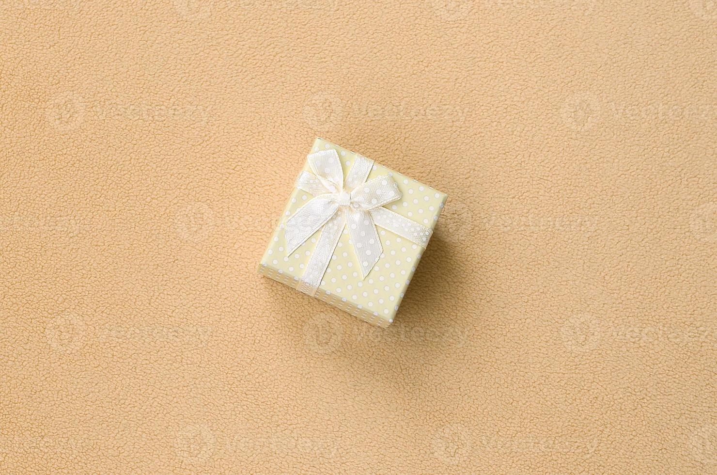 A small gift box in orange with a small bow lies on a blanket of soft and furry light orange fleece fabric. Packing for a gift to your lovely girlfriend photo