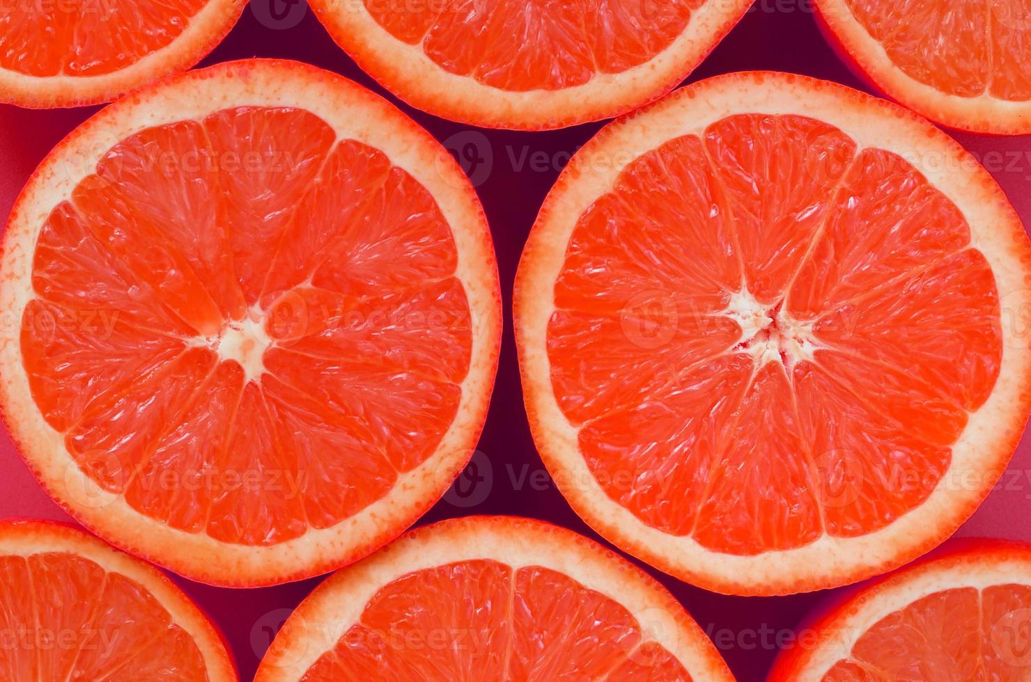 Top view of a several grapefruit slices on bright background in pink color. A saturated citrus texture image photo
