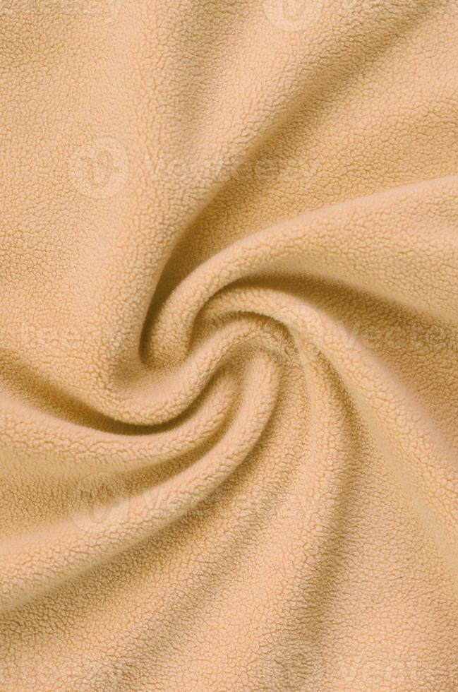The blanket of furry orange fleece fabric. A background of light orange soft plush fleece material with a lot of relief folds photo