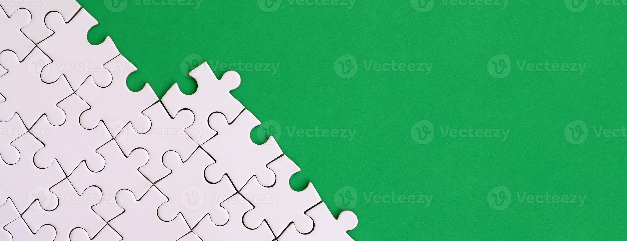 Fragment of a folded white jigsaw puzzle on the background of a green plastic surface. Texture photo with copy space for text